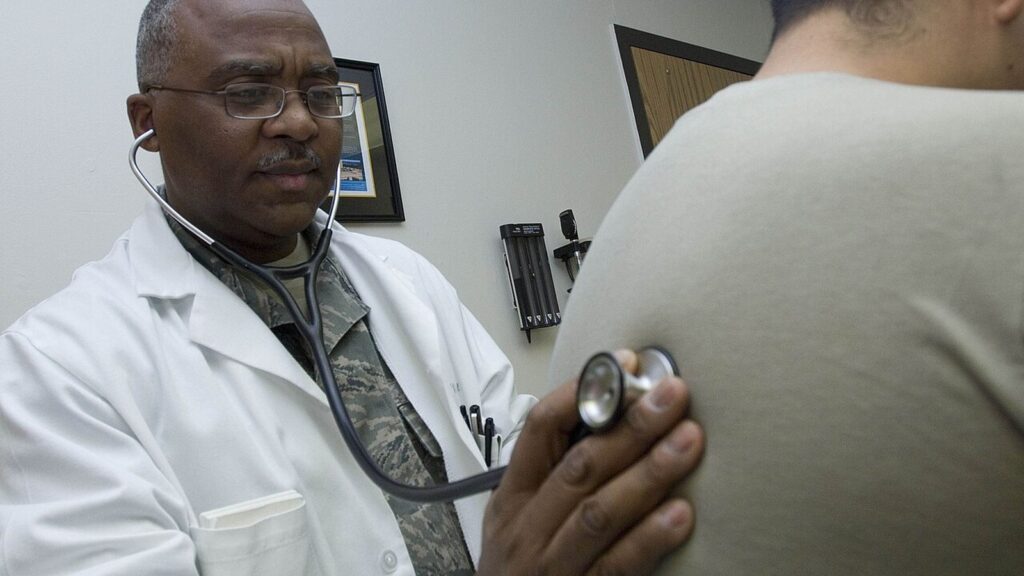 A doctor in a white coat listens to a patient's breathing with a stethoscope